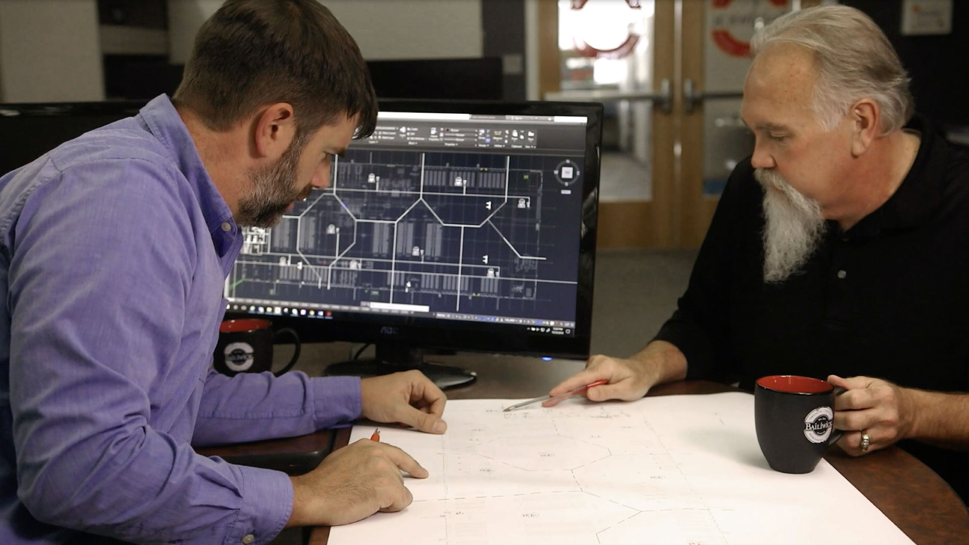 Two Bailiwick employees working on a floor plan with CAD designs on computer