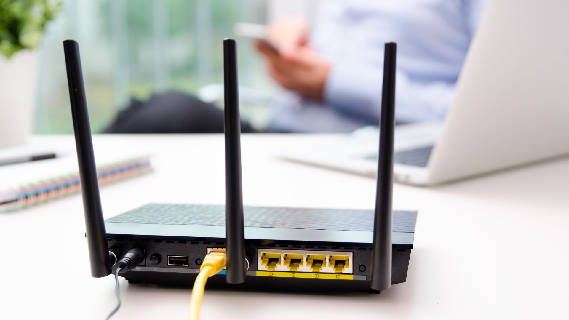 A wireless router on a desk with a man using his phone in the background.