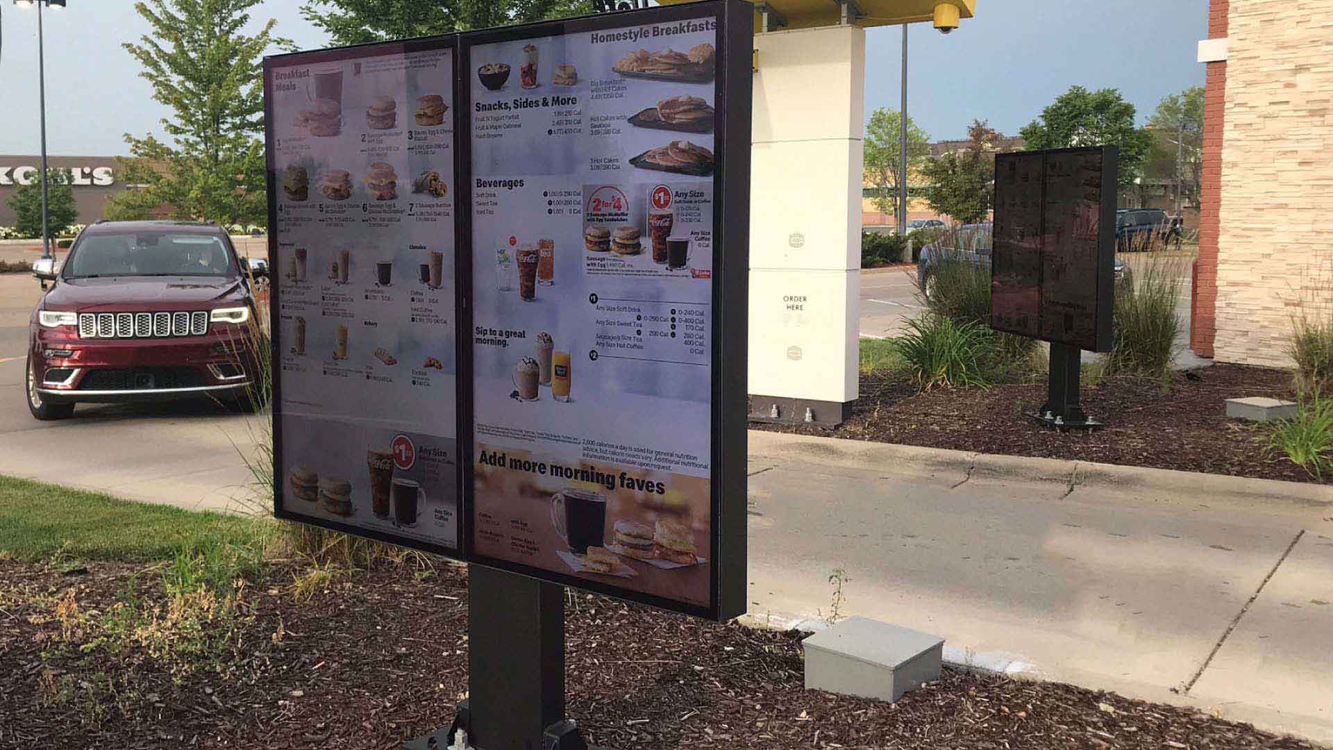 Outdoor digital menu board at a drivethru with car driving up.