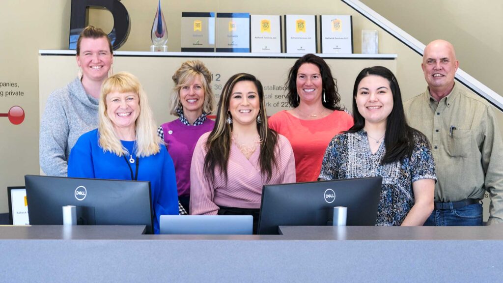 Bailiwick employees smiling at the front desk of the HQ.