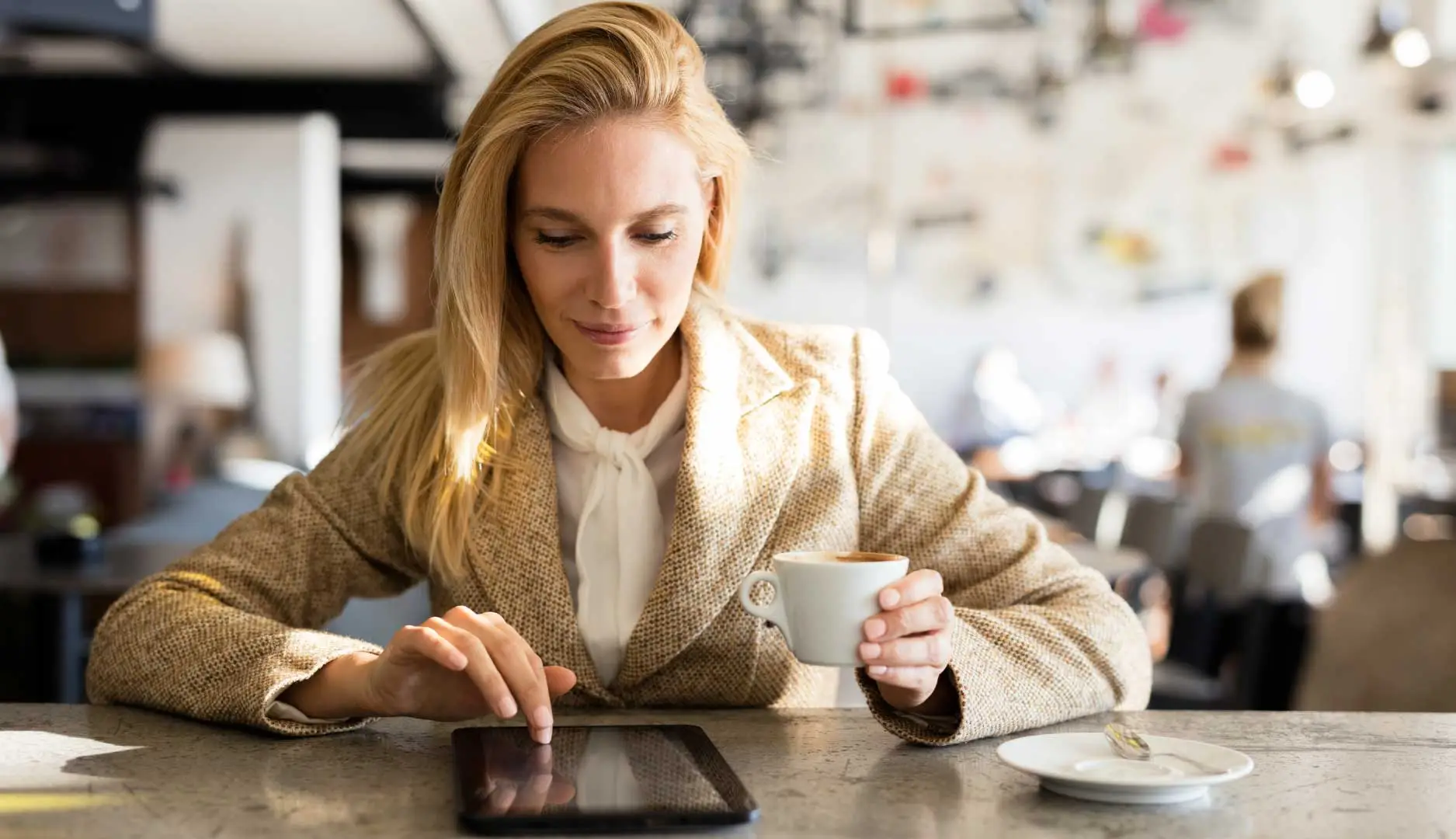 Woman reading news on her tablet while drinking coffee.