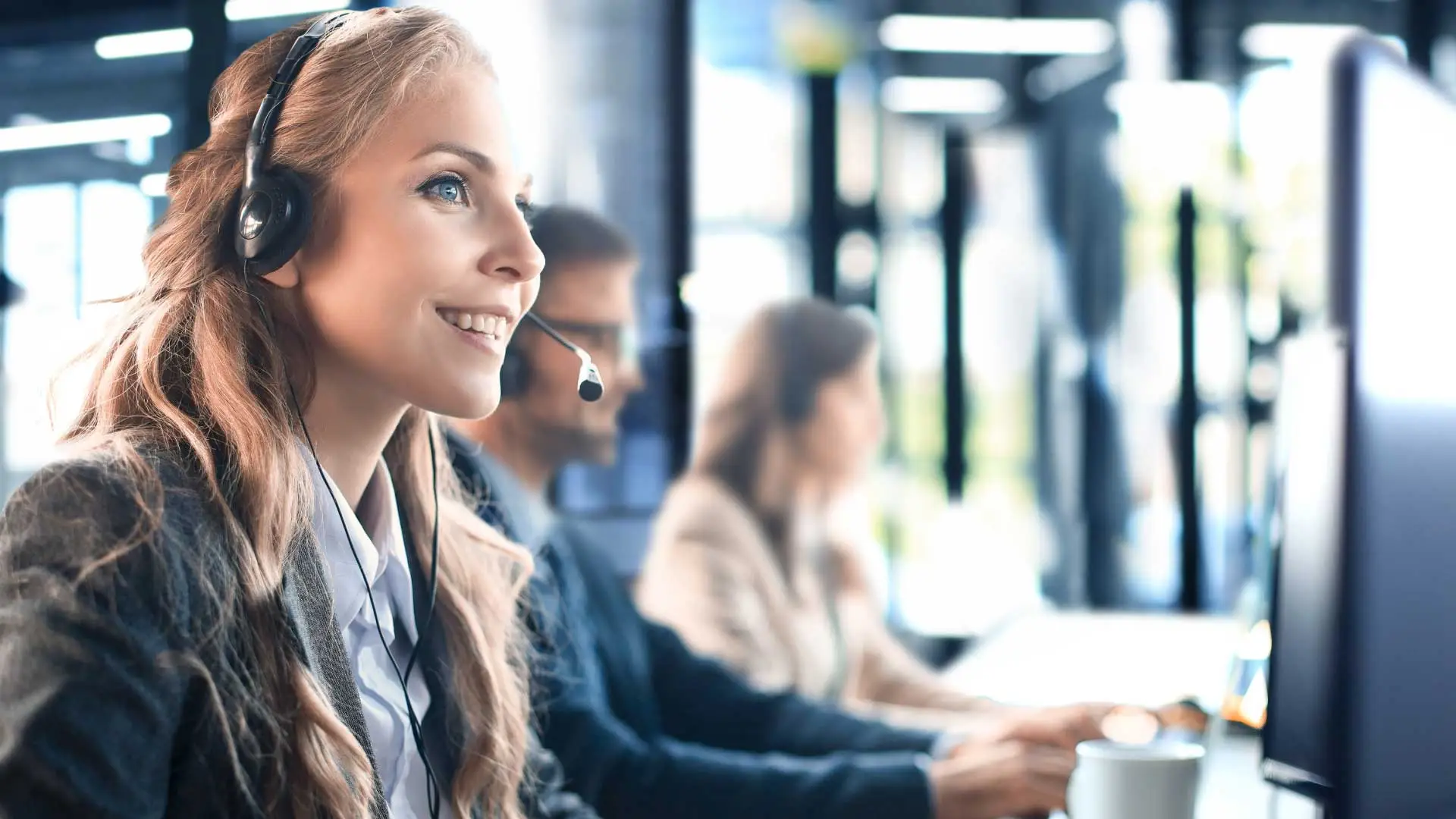 Smiling woman wearing headset sits at a support desk.