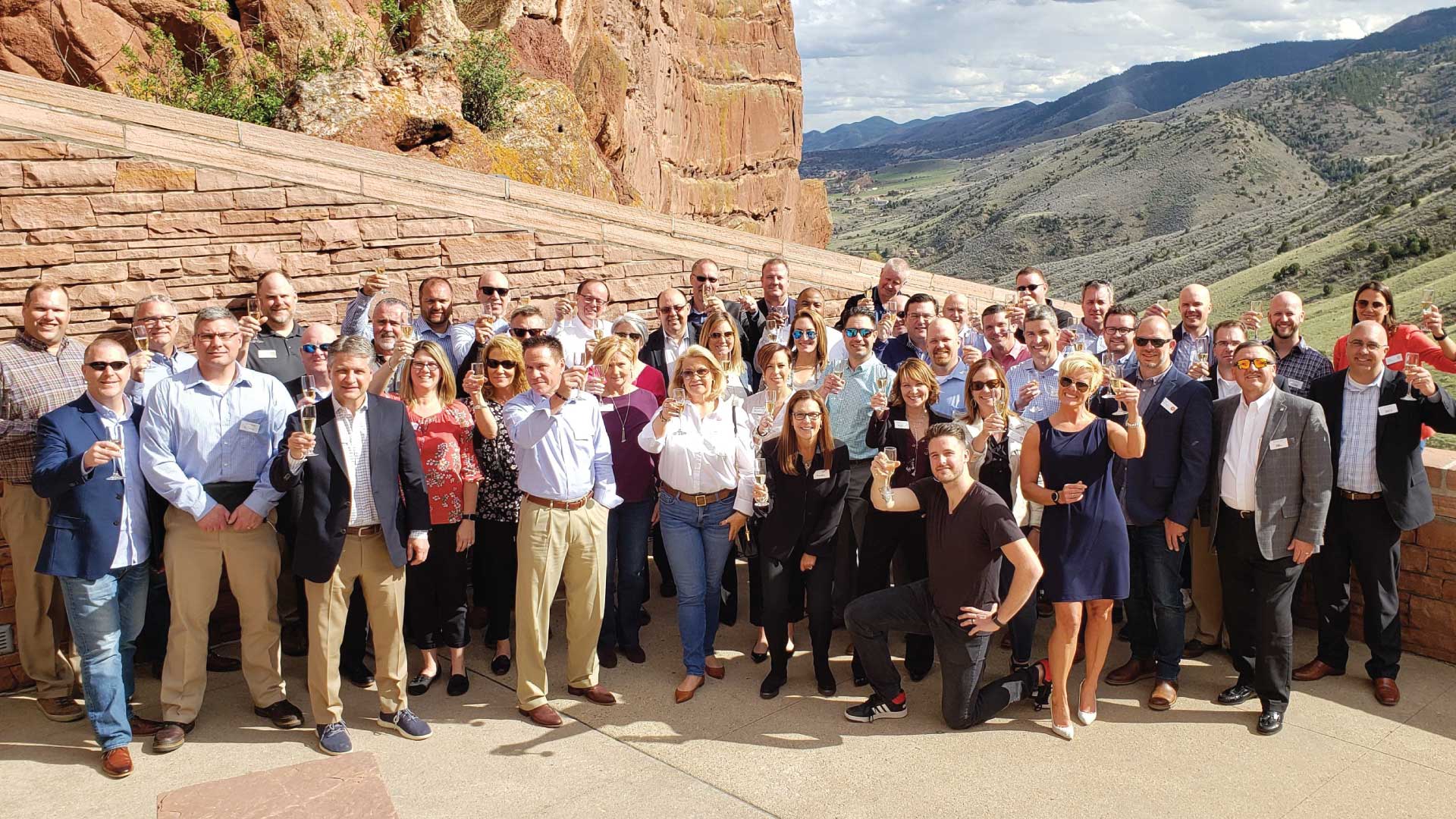 Group of people toasting to the camera while outside at Red Rocks in Colorado.