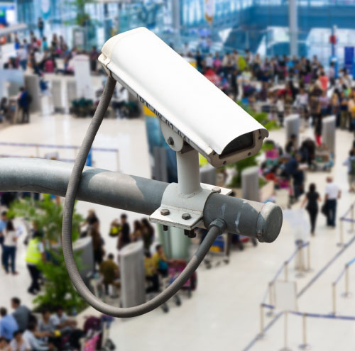 An older CCTV camera looking on a crowd of people.